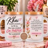Two frosted glass mugs with bamboo lids and clear straws, displayed on a marble surface in a styled home setting. One mug features the text 'Khai wasn't created to fit in.