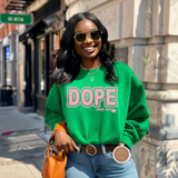 Woman wearing a green 'DOPE' sweatshirt on a city street.