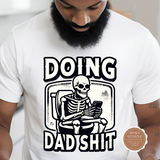 A man with a beard wearing a white crew neck t-shirt with the text 'DOING DAD SHIT' and an image of a skeleton holding a mobile phone.