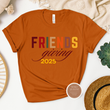 Orange t-shirt with 'FRIENDS giving 2025' text on a white surface with decorative items.
