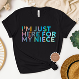 A black t-shirt with the text 'I'M JUST HERE FOR MY NIECE' displayed on it, laid out flat with decorative items around it.