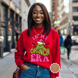 Woman wearing a red sweatshirt with 'In My Grinch Era' text on a city street.