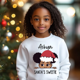 Child wearing a white sweatshirt with a graphic and text, standing in front of a decorated Christmas tree.