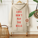 Beige hoodie with 'LOVE DON'T PAY THE BILLS' text on a hanger in a room setting.