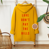 Yellow hoodie with 'LOVE DON'T PAY THE BILLS' text on a hanger against a white wall.