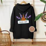 A black hoodie with a graphic design that includes a middle finger gesture and floral elements, displayed on a hanger with a 'F*CK OFF' text addition, placed against a wicker background with a plant and a wooden object in the background.