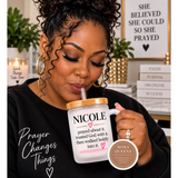 A woman in a black sweatshirt sipping from a frosted glass mug with a wooden lid. The mug has the name 'NICOLE' and a pink heart with the quote 'prayed about it, trusted God with it, then walked boldly into it.