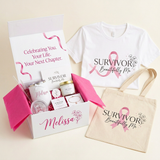 A curated gift set arranged on a light beige background, featuring an open white gift box with pink tissue paper and wellness items, a white T-shirt with a pink ribbon and the words 'SURVIVOR Beautifully Me,' and a beige tote bag with matching pink ribbon and text.