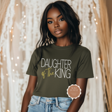 Woman wearing a green t-shirt with 'Daughter of the King' text, standing against a decorative background.