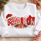 White toddler crewneck sweatshirt flat lay with the name Madison in festive embroidered-look patch letters with a Santa hat, red bow, and gingerbread man