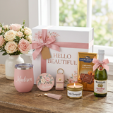 Hello Beautiful gift box tied with a pink bow beside the Madison tumbler, candle, floral mirror, tassel sanitizer keychain, full-size Ghirardelli caramel candy bar, and mini Martinelli's Sparkling Cider
