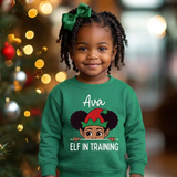 Toddler girl wearing a green personalized Christmas sweatshirt with the name Ava and a peeking elf girl above the words Elf In Training