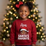 Toddler girl wearing a red personalized Christmas sweatshirt with the name Ava above the words Santa's Favorite