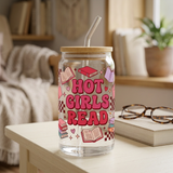 Hot Girls Read glass with bold pink and red lettering, book artwork, bamboo lid and glass straw beside reading glasses.