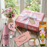 Strong As A Mother gift box tied with a white bow beside the water bottle, mirror, keychain, pouch, candle, Ghirardelli bar, and mini cider