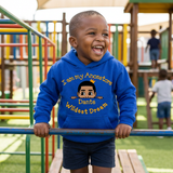 Laughing Black toddler boy on playground bars wearing a royal blue I Am My Ancestors Wildest Dream hoodie with the name Dante