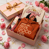 Blush pink gift box with gold ribbon filled with a Special Girl Real Good Girl hoodie, affirmation tumbler, and matching tote bag, styled with pink roses