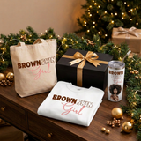 Brown Skin Girl Christmas Gift Box with a gold bow beside the sweatshirt, tote, and white matching tumbler