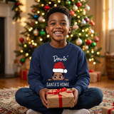 Smiling boy holding a Christmas gift wearing a navy Santa's Homie personalized sweatshirt by the tree