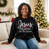 Black woman seated in a black Jesus Is the Reason for the Season sweatshirt with white text and a red heart.