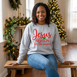 Black woman seated on a wooden bench in a gray Jesus Is the Reason for the Season sweatshirt with red text.
