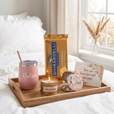 Hello Beautiful self-care tray with the Madison tumbler, lit Pink Champagne candle, full-size Ghirardelli caramel candy bar, floral mirror, and postcard on white bedding