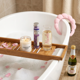Spa bath caddy across a bubble bath with a lit Champagne Toast candle, Dr Teal's lavender bath salts, and a Nicole champagne flute filled with cider