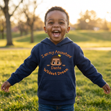 Giggling Black toddler boy in a park wearing a navy I Am My Ancestors Wildest Dream hoodie personalized with the name Dante