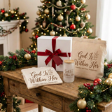 God Is Within Her Christmas Gift Box with a red bow beside the matching folded shirt, cup, and tote