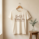 God Is Within Her cream t-shirt on a wooden hanger against a cream wall