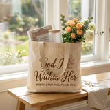 God Is Within Her tote bag on a bench by a window filled with a devotional, glass can cup, and flowers