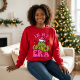 Black woman wearing a red In My Grinch Era Christmas sweatshirt beside a warmly lit Christmas tree.