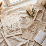 God Is Within Her matching shirt, frosted can cup, and tote flat lay on linen with a devotional journal