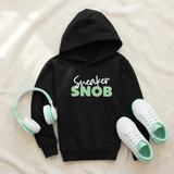 Black Sneaker Snob kids hoodie flat lay with mint print, white sneakers, and headphones