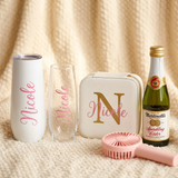 Close-up of the personalized Nicole champagne tumbler, glass flute, and gold monogram jewelry case with a mini Martinelli's and pink fan