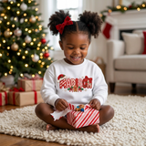 Lifestyle photo of a toddler girl unwrapping a Christmas gift wearing a white sweatshirt with the name Madison in embroidered-look patch letters