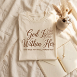 God Is Within Her shirt flat lay on linen with a devotional journal and gold cross necklace