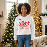 Black woman standing in a white Jesus Is the Reason for the Season sweatshirt with red text and a green heart.