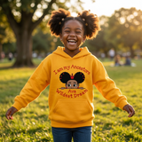 Laughing Black girl with afro puffs twirling in a park wearing a gold I Am My Ancestors Wildest Dream hoodie with the name Ava