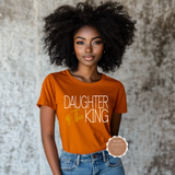 Woman wearing an orange 'Daughter of the King' t-shirt against a textured wall.